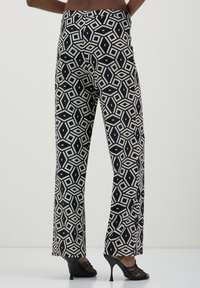 Pantaloni a gamba larga con un motivo geometrico a rombi in bianco e nero, realizzati in tessuto leggero con una texture liscia.