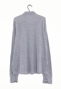 Camicia grigia a maniche lunghe appesa al contrario a un appendiabiti, con colletto e polsini imbottiti, dalla consistenza morbida e dal taglio comodo.