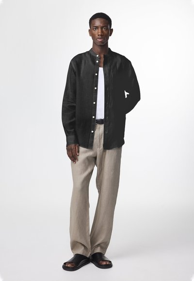 Svart långärmad skjorta med knapp-down krage, vit linne t-shirt under, beige linnebyxor och svarta sandaler med bred rem.
