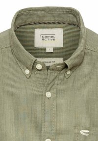 Olivengrøn kordfløjlsskjorte med button-down krave, der har en lille frontlomme, hvide knapper og et struktureret ribbet mønster.