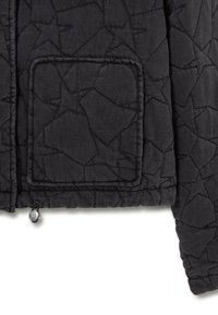 Veste matelassée noire avec un motif texturé abstrait, une poche carrée et un détail resserré avec un toggle argenté à l'ourlet.