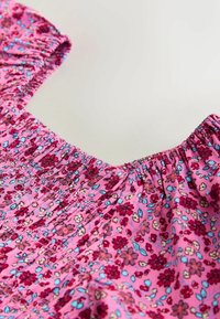 Rózsaszín anyag kis piros, kék és krémszínű virágmintával, összegyűrt varrással, valamint rugalmas nyakkivágással és ujjakkal.