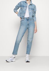 Světle modrá denimová bunda s knoflíkovým zapínáním, spárovaná s vysokým pasem světle modrými džíny. Pod tím bílá tričko a bílé tenisky.