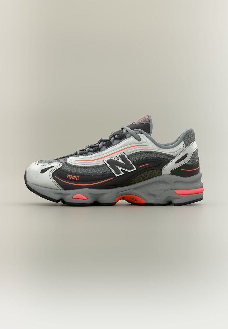 Baskets New Balance 1000 gris, noires et blanches avec des accents orange, lacets visibles et semelle épaisse sur un fond neutre.