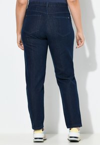 Tmavěmodré džíny s vysokým pasem, které mají dvě zadní kapsy a rovný střih nohavic, zkombinované se světlými teniskami.