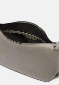 Borsa a tracolla in pelle grigia con una texture liscia, dotata di chiusura a zip e un interno nero con una piccola tasca e il logo del marchio.