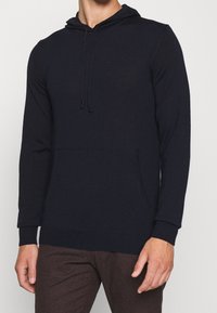 Marinblå hoodie med lång ärm, framficka, ribbad mudd och fåll, tillverkad av ett mjukt, strukturerat tyg.