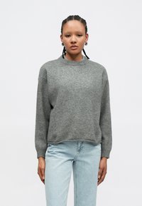 Gray knit sweater with a round neckline, long sleeves, and a relaxed fit, paired with light blue denim jeans. Soft texture and minimal design.