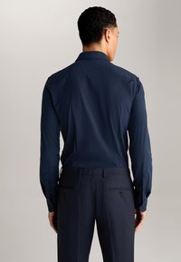 Marineblauw overhemd met lange mouwen, voorzien van een gladde textuur, knoopmanchetten en een gestructureerde kraag, gecombineerd met donkere broeken met achterzakken.