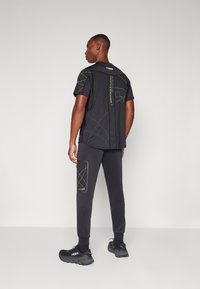 Sort athletic t-shirt med geometriske linjer og detaljer, parret med mørke sweatpants med en sidelomme og kontraststikning.
