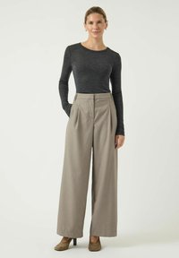 Zwarte lange mouwen top, hooggeplaatste beige wijde broek en tan hoge hakken. De broek heeft voorplooien en zijzakken.