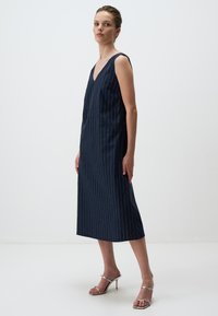 Navy gestreepte jurk met een V-hals en een mouwloos ontwerp, gemaakt van een textuurstof, die tot halverwege de kuit valt, gecombineerd met zilveren hoge hakken sandalen.