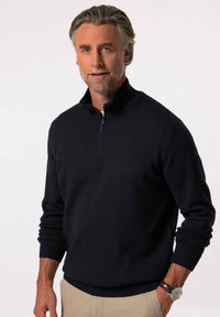 Suéter navy con cremallera y cuello alto, puños y dobladillo acanalados. Presenta una textura suave y un corte relajado. Se lleva con pantalones de color claro.