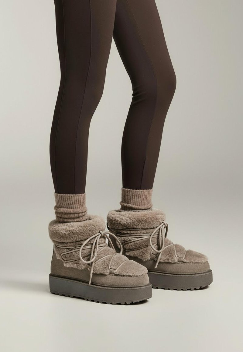 Cizme de iarnă din fleece bej, cu talpă groasă gri, design strâns în jurul gleznei, închidere cu șiret și finisaj moale, texturat.