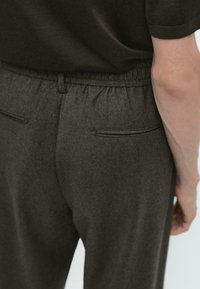 Pantaloni della tuta grigio scuro con vita elastica, dotati di due tasche posteriori e un tessuto morbido e testurizzato. Design semplice e minimalista.