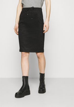 Person wearing a black knee-length skirt with a tied waistband, gray top, and black lace-up platform boots, standing against a plain background.