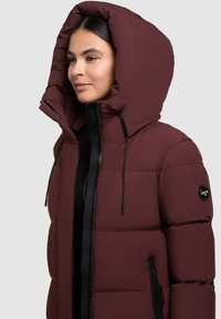 Burgundy színű puffermellény, nagy kapucnival, cipz�áros elejével és állítható húzókkal. Jellemzője a logó folt és az oldalsó cipzáros zsebek.