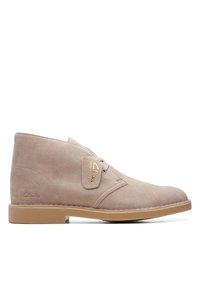 Beige mocka chukka stövel med rund tå, minimal ögla och en tan gummisula. Har ett präglat logotyp och läderetikett på sidan.