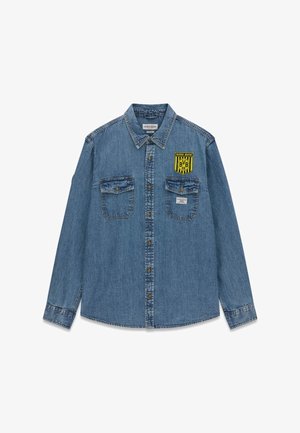 Blauw denim overhemd met knopen, twee borstzakken, een gele "BVB 09" badge op de rechterborst en een "Guess Jeans" label boven de linkerzak.