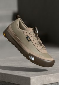 Light brown athletic shoe with a textured upper, brown rubber sole, and logo. Features laces and a reinforced toe cap for durability.