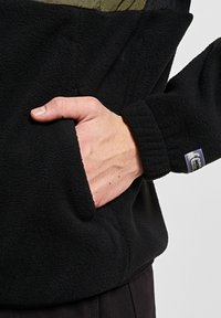 Svart fleece genser med en olivengrønn panel, som har en frontlomme og ribbestrikkede ermer. Strukturert stoff med en avslappet passform.