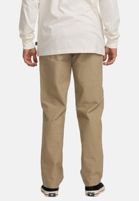 Khaki cotton pants with a relaxed fit, visible stitching, and slanted front pockets. Worn with black sneakers, showcasing a casual look.