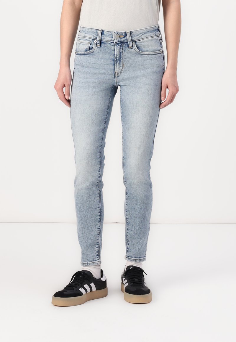 Jeans skinny de color azul claro con una cintura alta, diseño clásico de cinco bolsillos y un ligero desgaste. Combinados con zapatillas negras con rayas blancas.