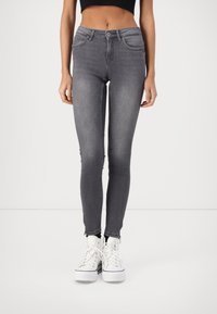 Jeans ajustados en denim gris oscuro, con una cintura de altura media, bolsillos frontales y dobladillos desgastados. Combinados con zapatillas altas blancas.