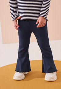 Pantalones acampanados con textura acanalada en azul marino y dobladillo ondulado, combinados con zapatillas blancas. La parte superior tiene franjas horizontales en azul marino y blanco.