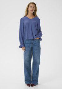 Lavender long-sleeve blouse with a V-neck, relaxed fit, and gathered cuffs, paired with high-waisted, wide-leg blue denim jeans.