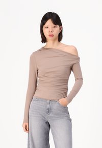 Top cu mâneci lungi, off-the-shoulder, dintr-un material bej moale, cu detalii pliate; asortat cu blugi gri cu talie înaltă.