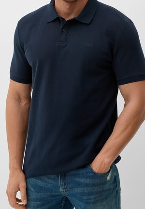 Polo azul marino de tela texturizada, con cuello de solapas y una tapeta con tres botones. Corte informal y combinado con vaqueros azules.