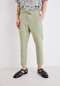 Helle grüne, taillierte Hose aus einem weichen Stoff mit einem elastischen Bund und Seitentaschen. Kombiniert mit schwarzen, geflochtenen Sandalen.