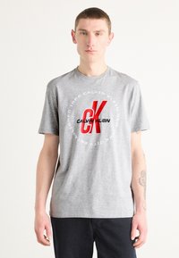 Gray short-sleeve t-shirt made of cotton, featuring a red "CK" logo in a circular graphic with text around it, casual fit.