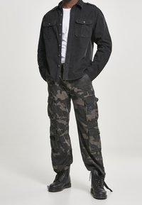 Svart skjorta med knappar och två bröstfickor, kombinerad med kamouflagebyxor med flera fickor, och svarta snörskor.