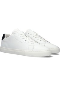 White leather sneakers with a smooth finish, round toe, flat rubber sole, and black heel accent. Features lacing, stitching details, and logo.