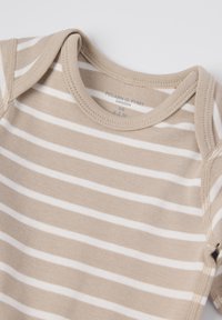 Beige katoenen body met witte horizontale strepen, voorzien van een drukknoopsluiting aan de onderkant en een ronde halslijn. Merklabel zichtbaar.