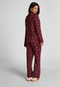 Bordeauxroze pyjamaset met lange mouwen en broek, voorzien van een wit patroon met kleine ontwerpen. Zachte stof met een ontspannen pasvorm en mouwen met boorden.