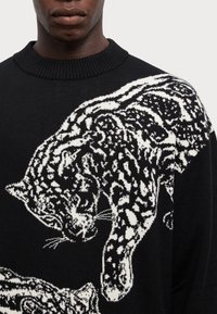 Maglione nero a maglia con un motivo leopardato bianco, dotato di un colletto a coste e un contrasto testurale distintivo nel design.