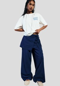T-shirt blanc avec un graphisme bleu, associé à un pantalon large bleu marine avec un design enroulé et un nouage en dentelle. Chaussures légères texturées incluses.