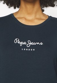 Tyrkysové bavlněné tričko s kulatým výstřihem a bílým logem "Pepe Jeans London" v kurzívě napříč hrudníkem. Hladká textura.