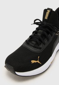 Baskets noires de sport avec une tige en maille, des détails texturés et un logo Puma doré. Elles sont dotées de lacets noirs et d'une semelle blanche.