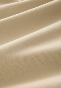 Beige bomuldsstof med en glat tekstur, der har subtile folder og et ensartet vævemønster over hele overfladen.