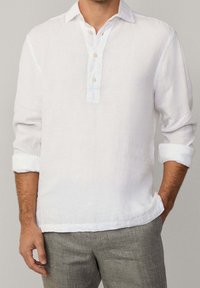Camicia in lino bianco con patta con bottoni, maniche lunghe arrotolate e vestibilità comoda. Tessuto leggero, design casual e leggero effetto lucido.