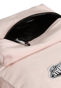 Rosa ryggsäck i manchester med dragkedja; insidan har svart foder och en metallisk penna syns inuti. Logotypmärke är tydligt synligt.