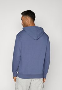 Hætte sweatshirt i en ensfarvet mørkeblå farve, med en kængurulomme og ribbede manchetter. Fremstillet af blødt, tekstureret stof.