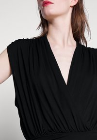 Robe noire avec un décolleté en V profond, des manches courtes avec des détails drapés et une taille froncée. Tissu lisse et léger avec une texture fluide.