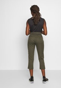 Pantalones cortos de color verde oliva, con cintura elástica, bolsillos laterales y textura suave. Combinados con calzado negro y una blusa sin mangas oscura.