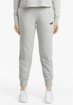 Onderlichaam, gekleed in lichtgrijze Puma joggingbroek en witte Puma sneakers, staand met handen ontspannen langs het lichaam tegen een witte achtergrond.