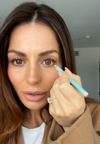 Ljusbrun ullkappa, turkos penna i handen, visar en hand med en silverknuten ring. Huden har en slät yta och naturlig smink.